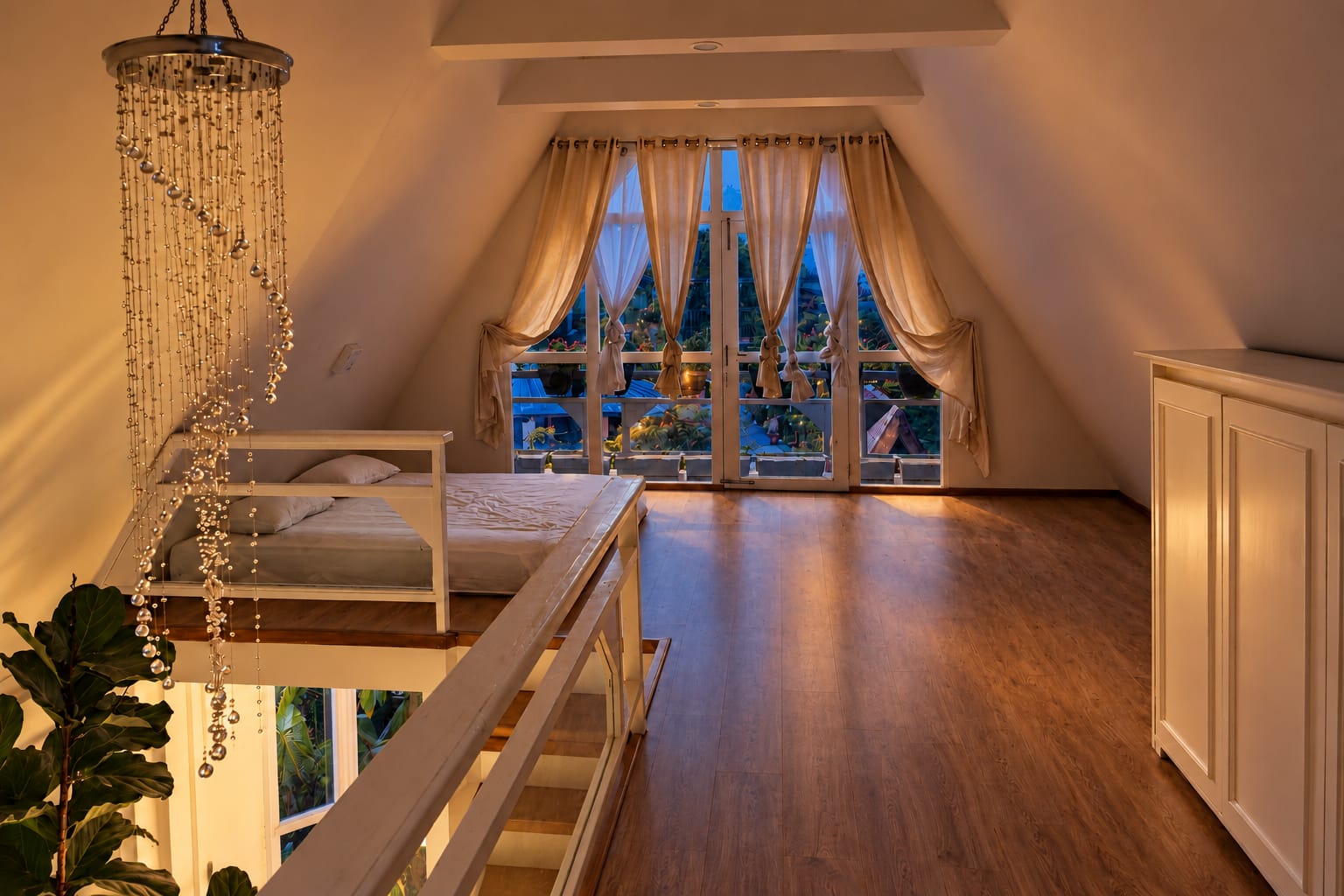 The homestay loft under the sloping roof: low bedding behind a white rail, a crystal chandelier and curtained glass doors